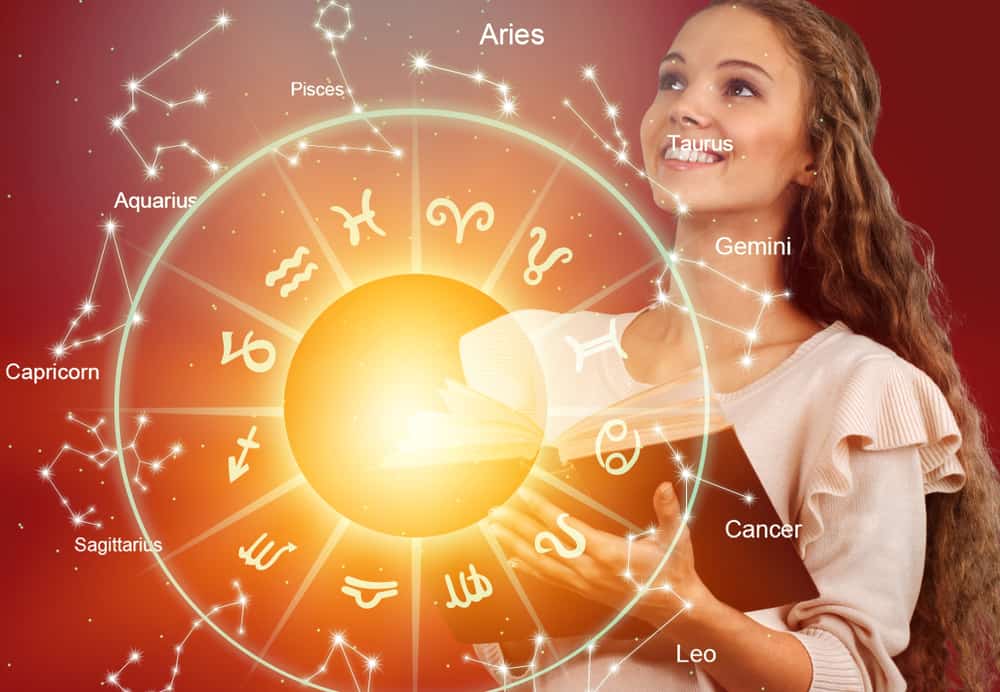 Horoskop med sol i bakgrunn og en kvinne som holder en bok ser fremover og smiler